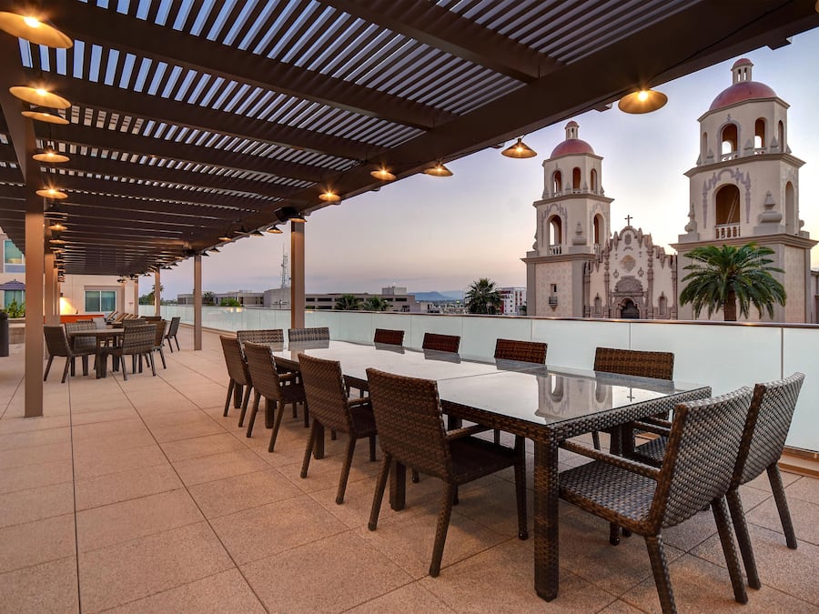 An outdoor patio with a long table and chairs, overlooking a historic building with two bell towers.