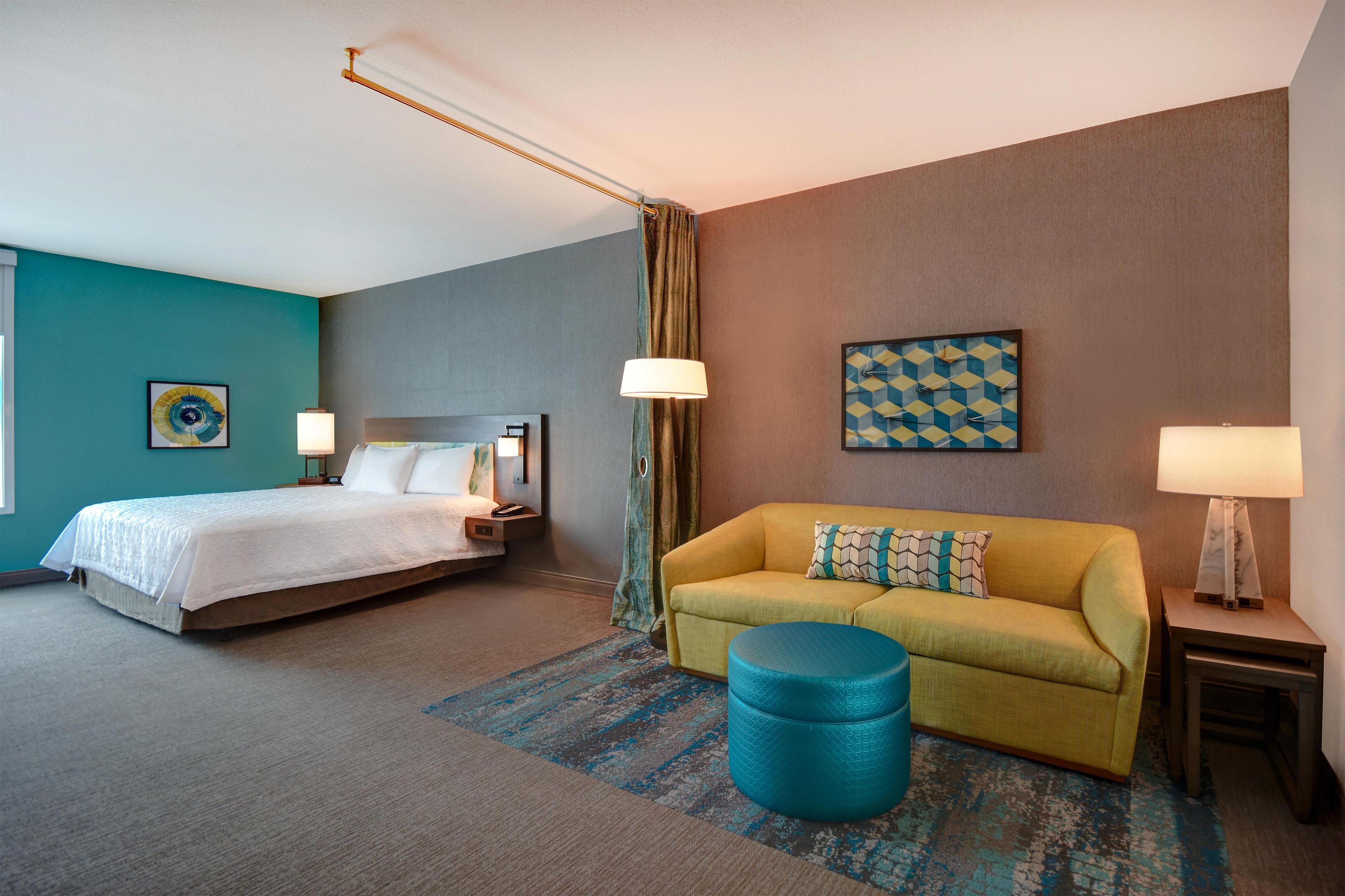 Una camera d'albergo con un letto, un divano, un poggiapiedi, una lampada e un quadro appeso al muro.