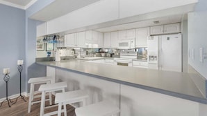 A modern kitchen with white cabinetry, a central island with stools, and a microwave.
