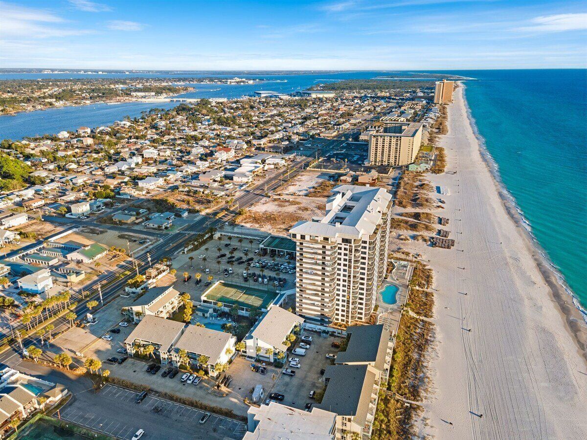 An aerial view of a coastal town with a beachfront hotel, a marina, and a dense residential area.