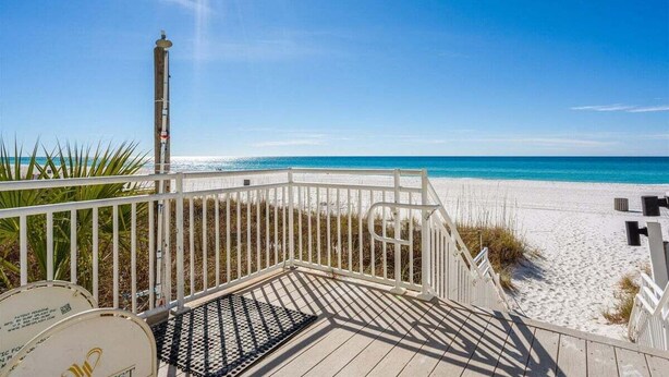 A wooden deck leading to a sandy beach with a clear blue sky.
