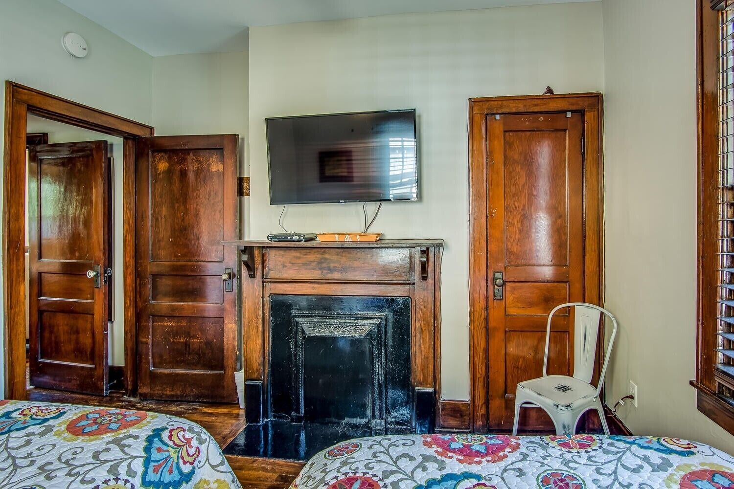 Quarto com lareira, televisão montada acima e duas portas de madeira.