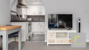 Una cocina moderna con armarios blancos, horno empotrado y un televisor de pantalla plana grande sobre una consola blanca.