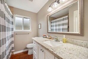A bathroom with a white toilet, a sink with a mirror, and a shower curtain. - Country-Chic Inspired Home - Mins from Everything! (Houston)