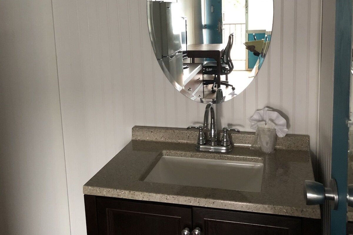 A bathroom with a round mirror, a sink, and a door with a towel rack.