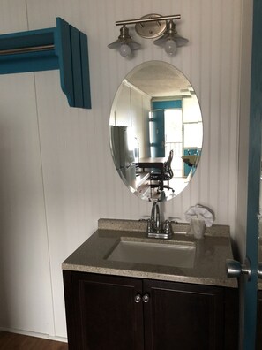 A bathroom with a round mirror, a sink, and a door with a towel rack. - Rodeway Inn Nashville (Nashville)