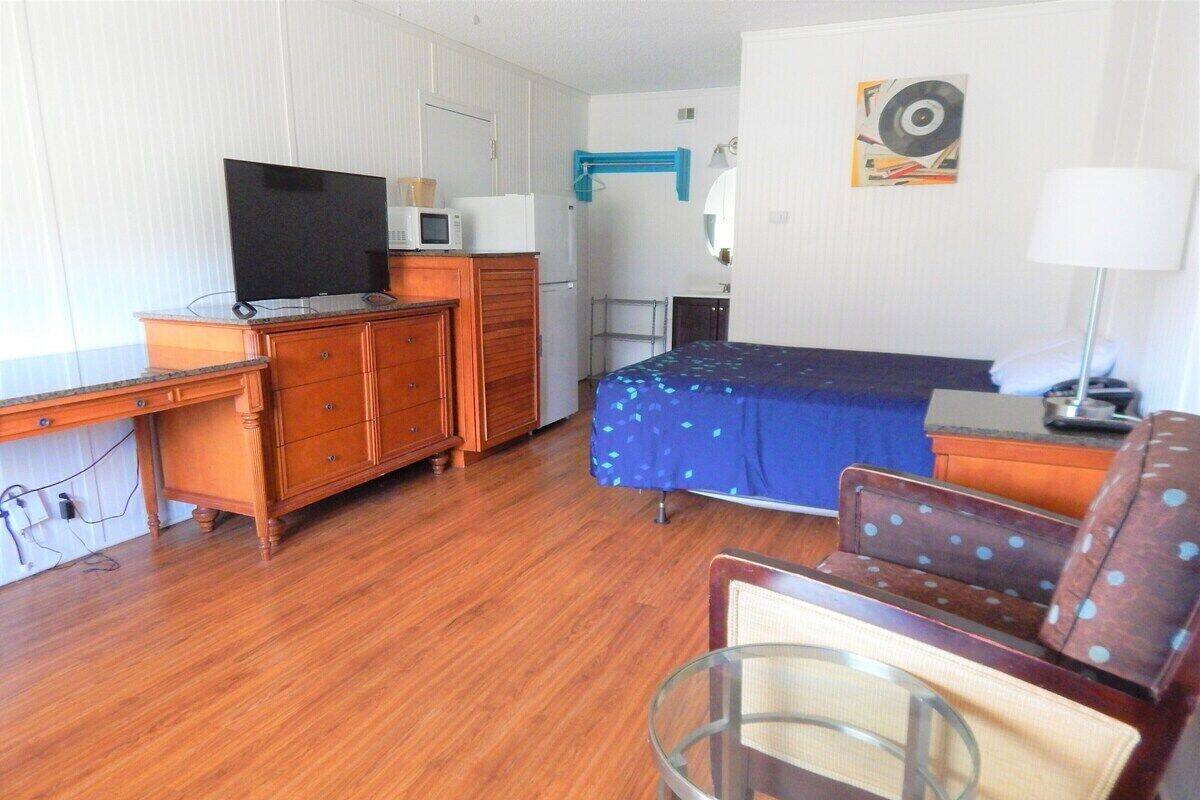 A room with a bed, a desk with a television, a chair, and a lamp.