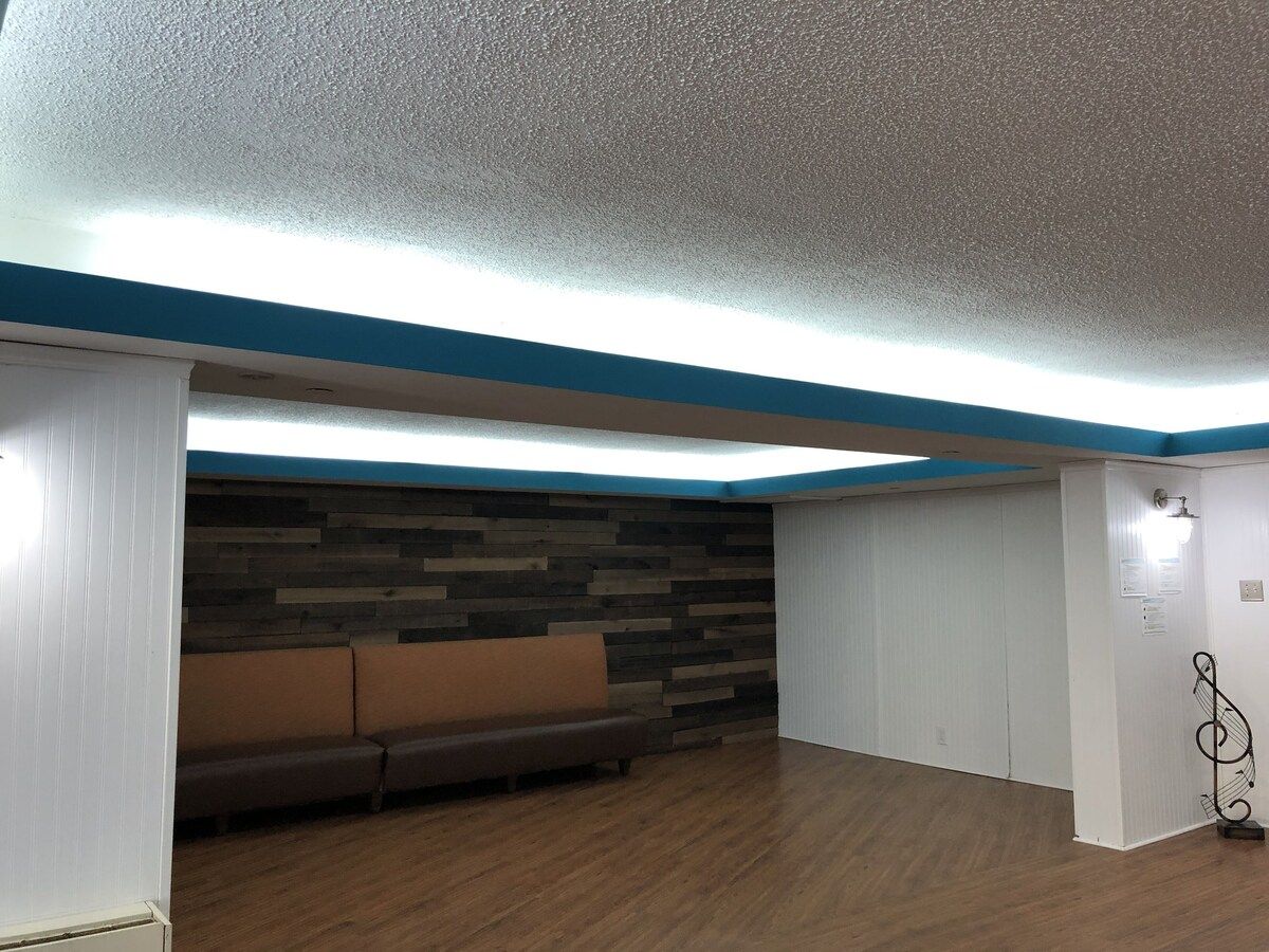 Una habitación con piso de madera, un sofá marrón, pared blanca con detalles azules y techo con textura.