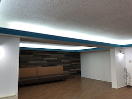 Una habitación con piso de madera, un sofá marrón, pared blanca con detalles azules y techo con textura.