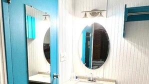 A bathroom with a blue door, a round mirror, a sink, and a towel rack. - Rodeway Inn Nashville (Nashville)