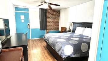 Habitación de hotel con cama, escritorio, silla, ventilador de techo y pared de ladrillo.