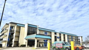 A multi-story building with a blue roof, a parking area, and a van with a sign. - Rodeway Inn Nashville (Nashville)