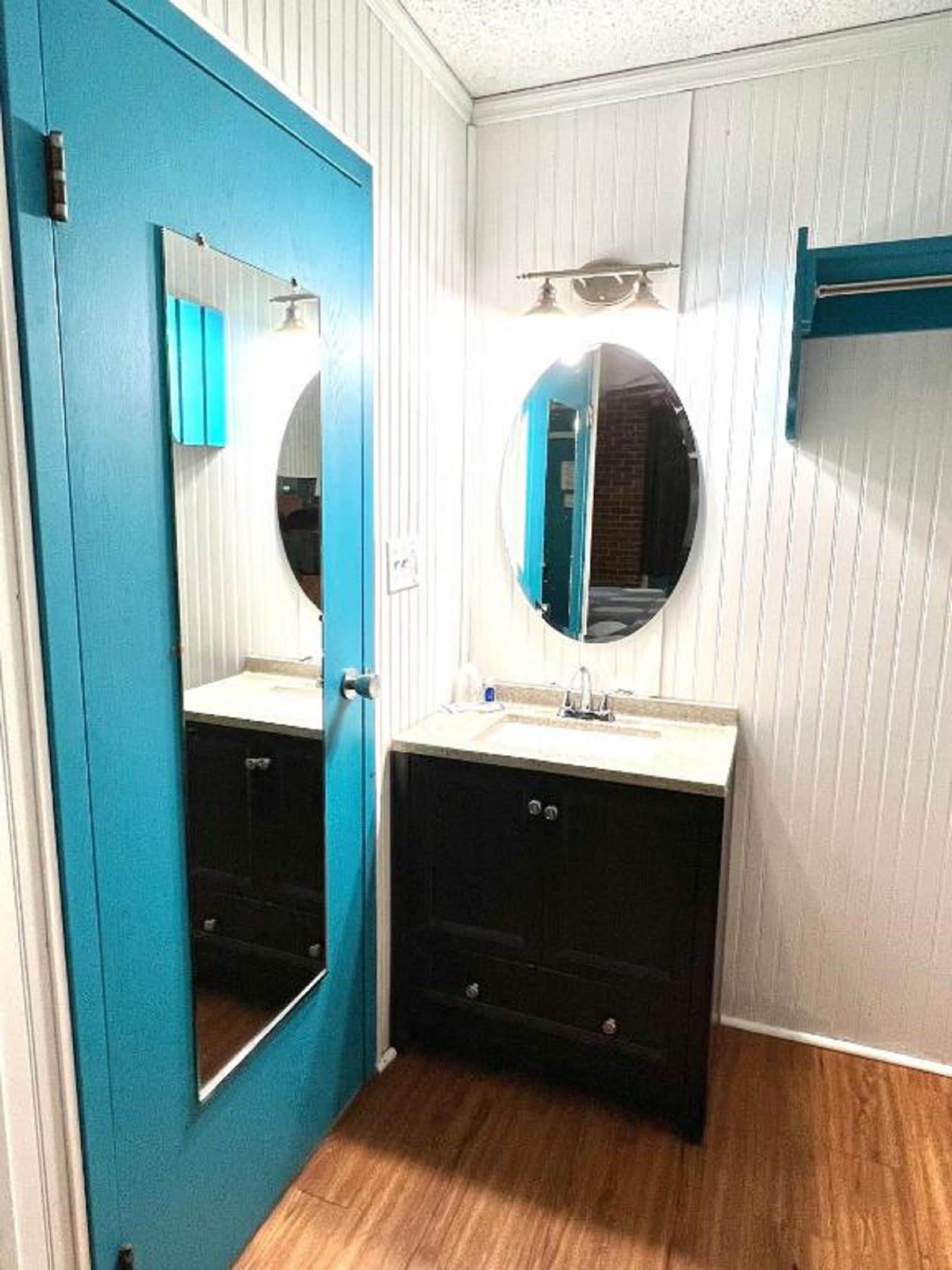Un baño con puerta azul, un espejo redondo, un lavabo y un perchero para toallas.