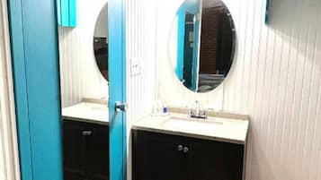 Un baño con puerta azul, un espejo redondo, un lavabo y un perchero para toallas.