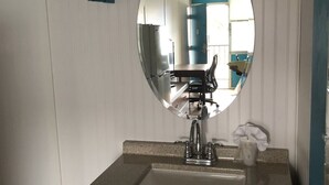 A bathroom with a round mirror, a sink, and a door with a towel rack. - Rodeway Inn Nashville (Nashville)