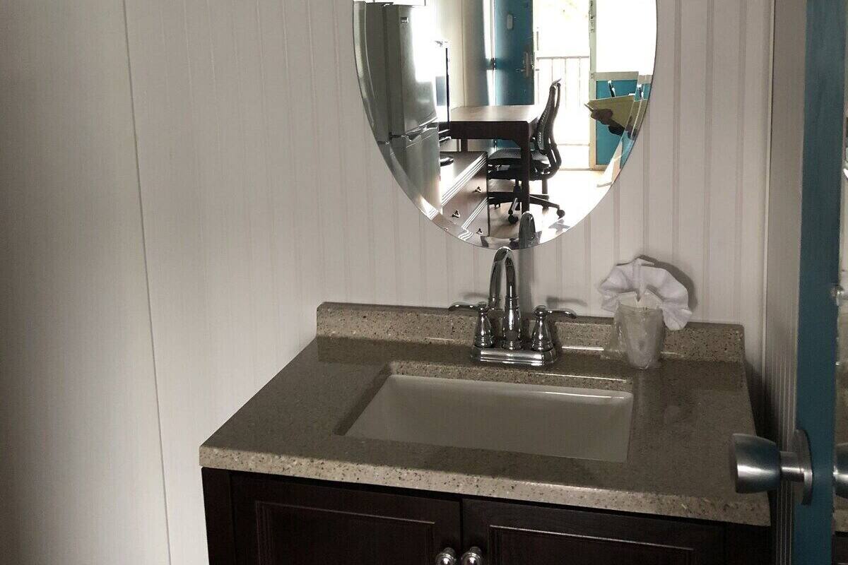 A bathroom with a round mirror, a sink, and a door with a towel rack.