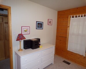Cozy room with a simple layout, featuring a dresser, lamp, and speaker.