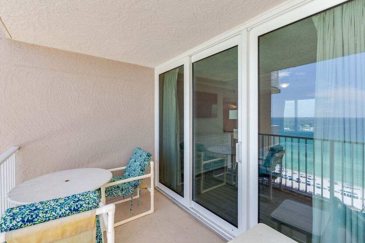 Een balkon met een witte tafel en stoelen, een schuifdeur en uitzicht op het strand.