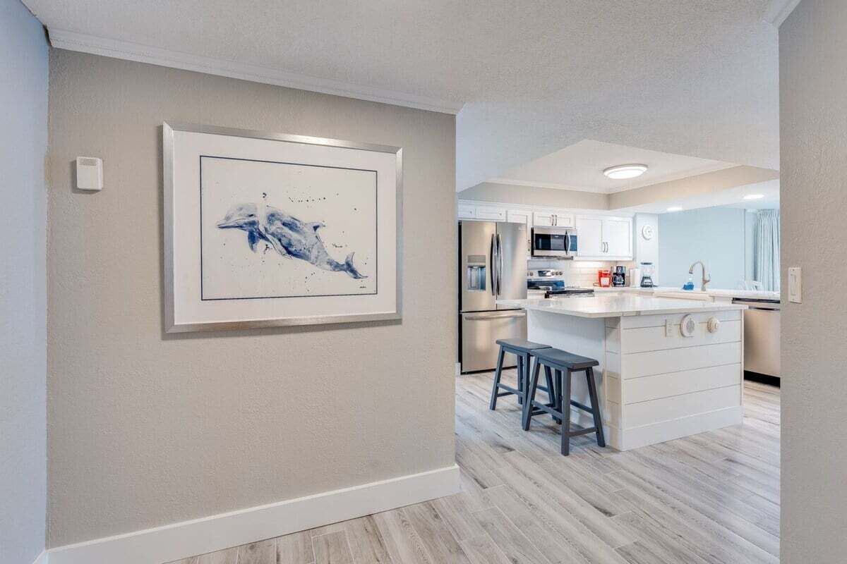 Une cuisine moderne avec des meubles blancs, un îlot central doté de tabourets et une œuvre d’art encadrée au mur.