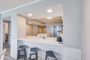 Una cocina moderna con una isla central, taburetes de bar y una licuadora integrada.