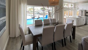 A spacious dining area with a view of a swimming pool, a kitchen with white cabinets, and a hanging woven light fixture. - Excellent home for multiple families.  Enjoy the pool or fish off the dock. (Clearwater)
