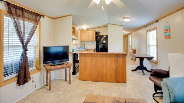 Un espacio habitable compacto con kitchenette, zona de comedor y televisor sobre un pedestal de madera.