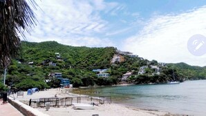 Une plage côtière avec des maisons construites sur une colline, une plage de sable et une mer calme.