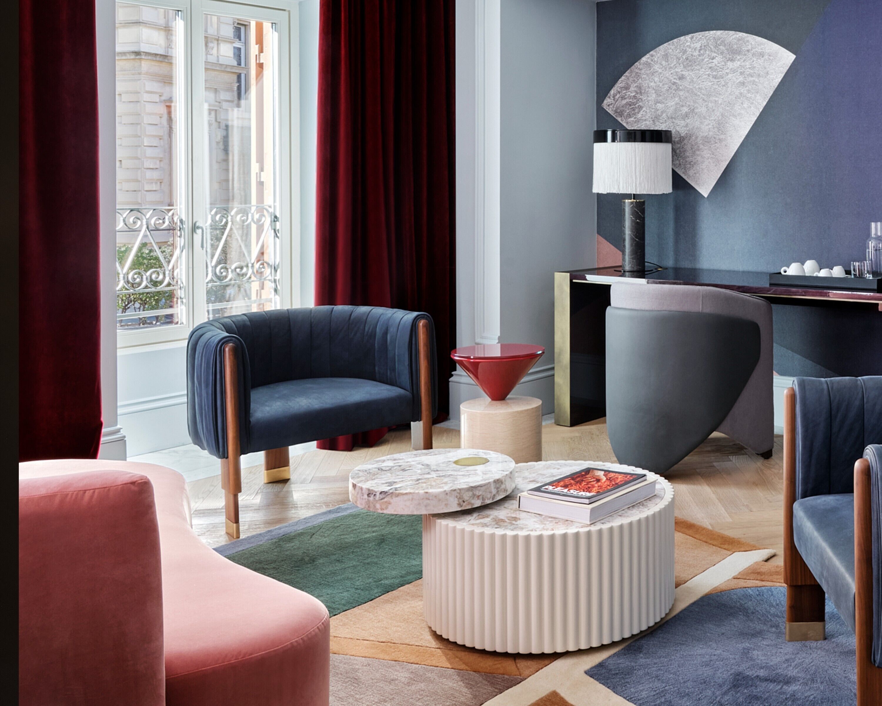A modern living room with a dark blue armchair, a red side table, and a round coffee table with a book.
