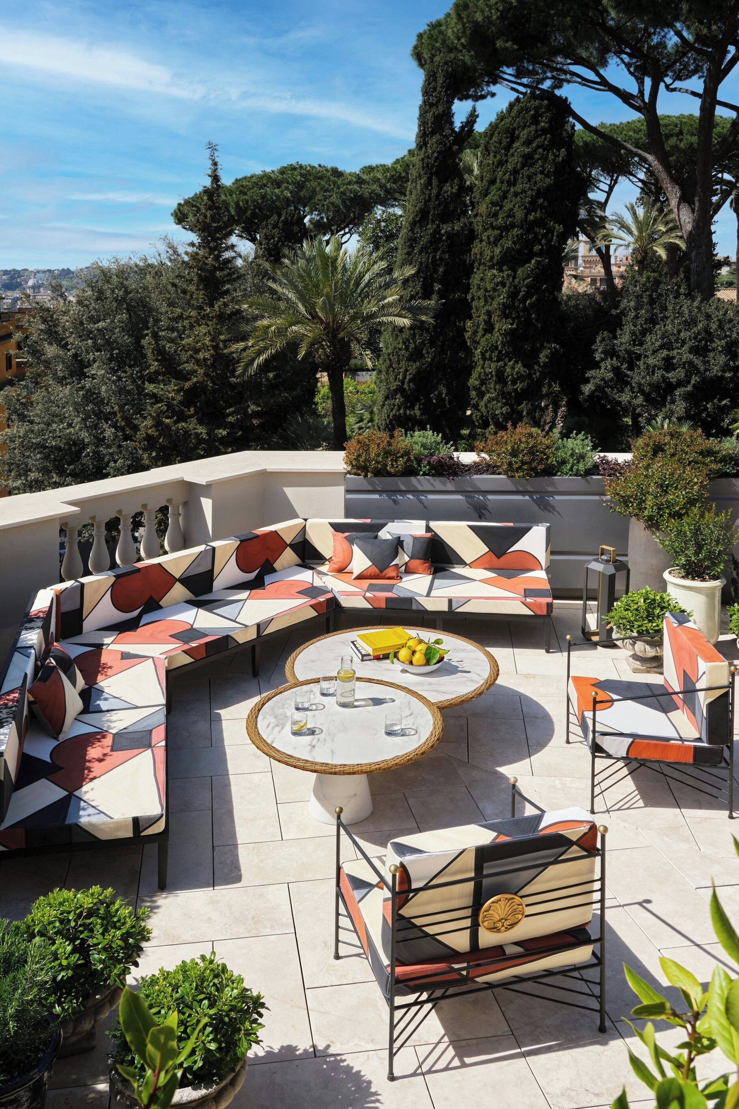 A sunlit outdoor seating area with a curved sofa, a round coffee table, and a small table with drinks.