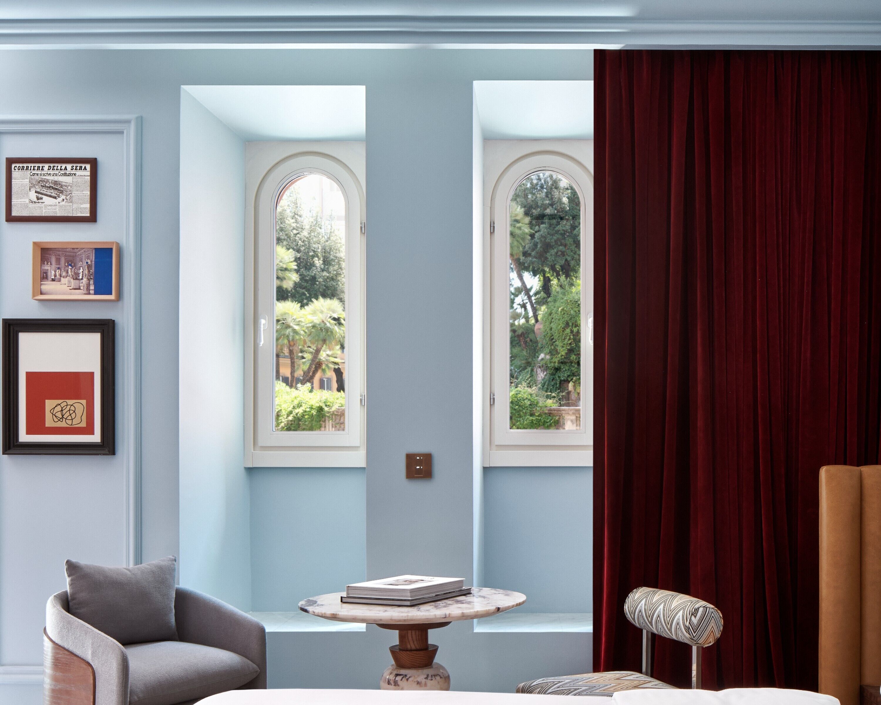 A room with two arched windows, a red curtain, a framed picture, a chair, and a small table with a book.