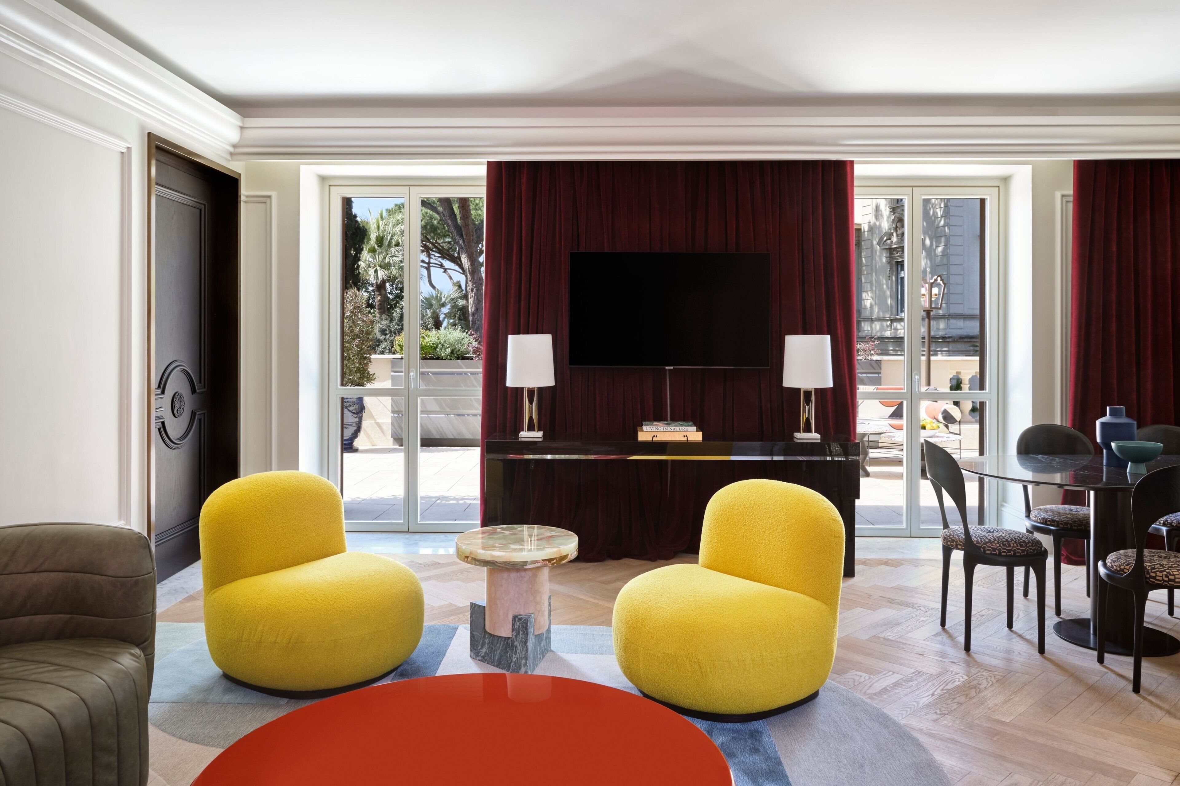 A modern living room with yellow armchairs, a red table, and a TV on a dark wall.