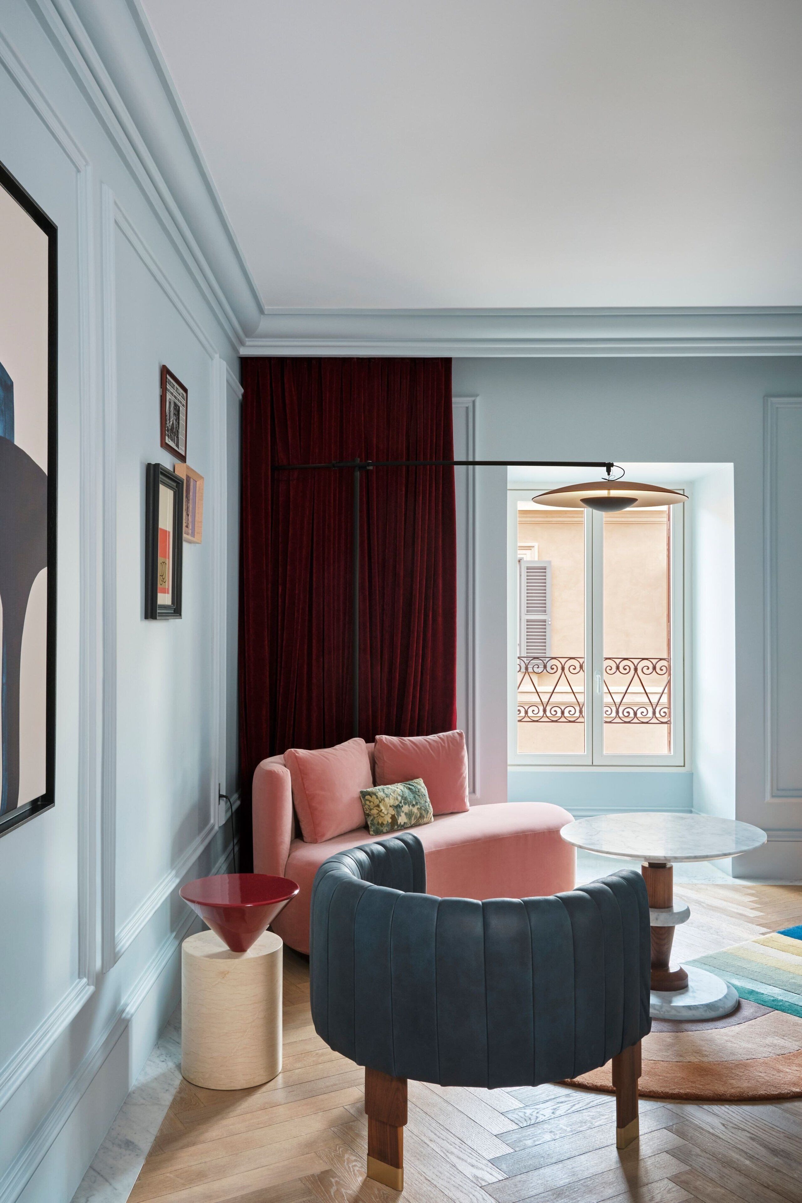 A room with a pink sofa, a blue armchair, a red side table, and a round coffee table.