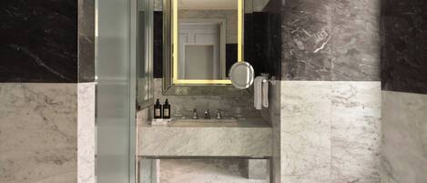 A bathroom with a marble vanity, a mirror, a towel rack, and a glass shower enclosure.