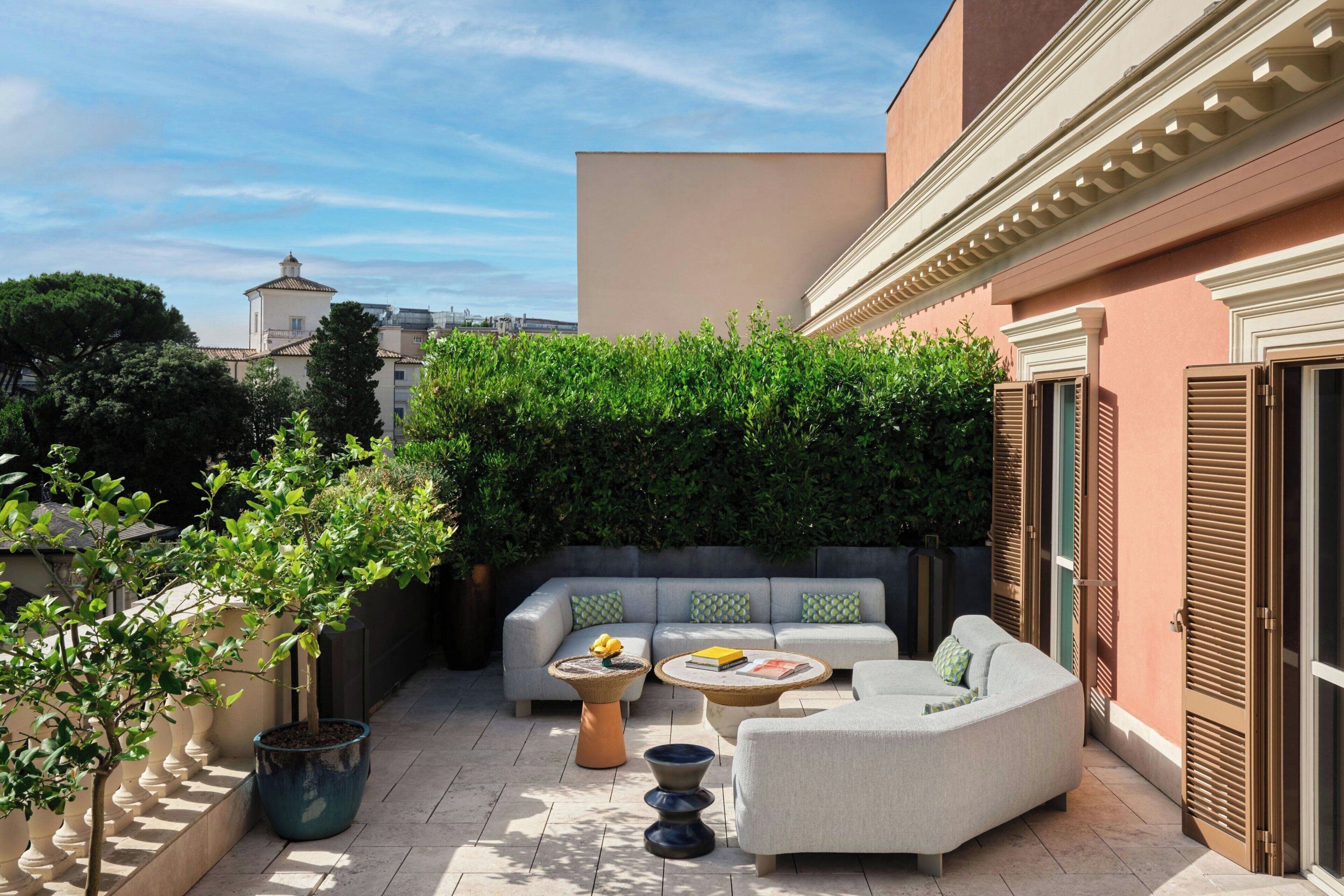 Un espace extérieur ensoleillé, aménagé avec un canapé, deux petites tables d’appoint et une plante en pot.