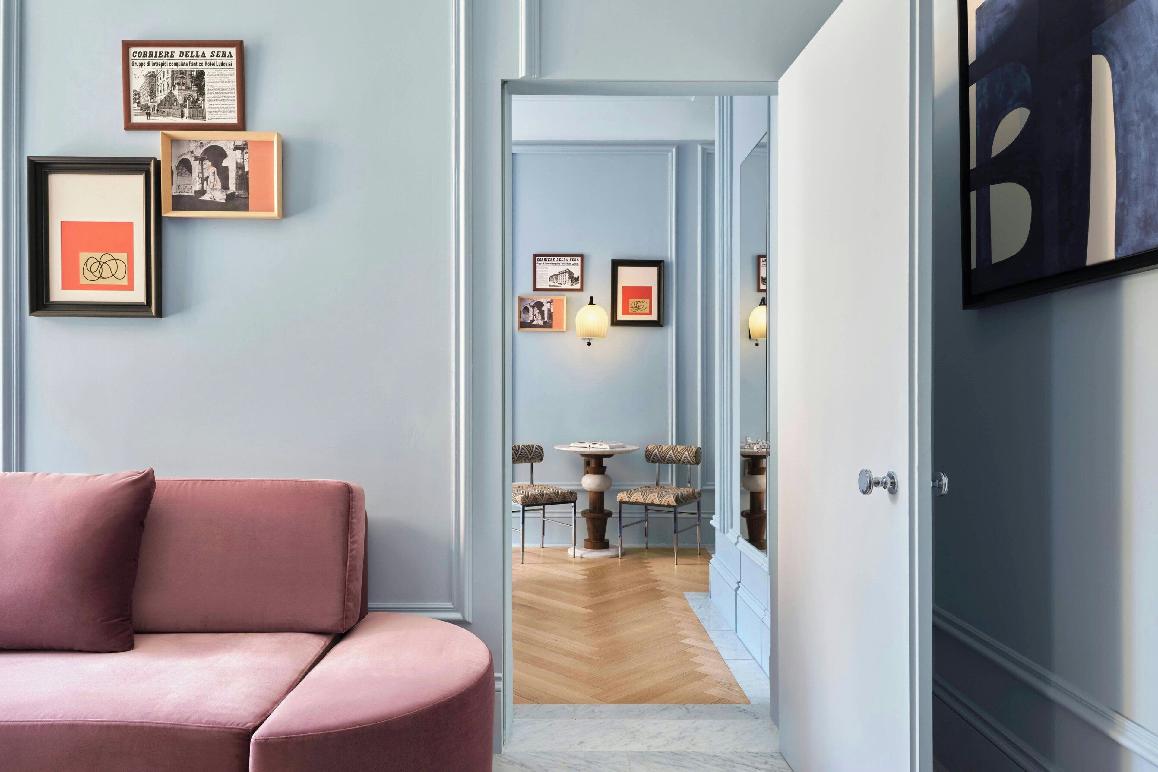 Un pasillo con un sofá rosa, cuadros en la pared y una zona de comedor con mesa y sillas.