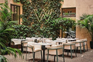 An outdoor café with tables and chairs, surrounded by lush greenery and a decorative wall. - W Rome (Rome)