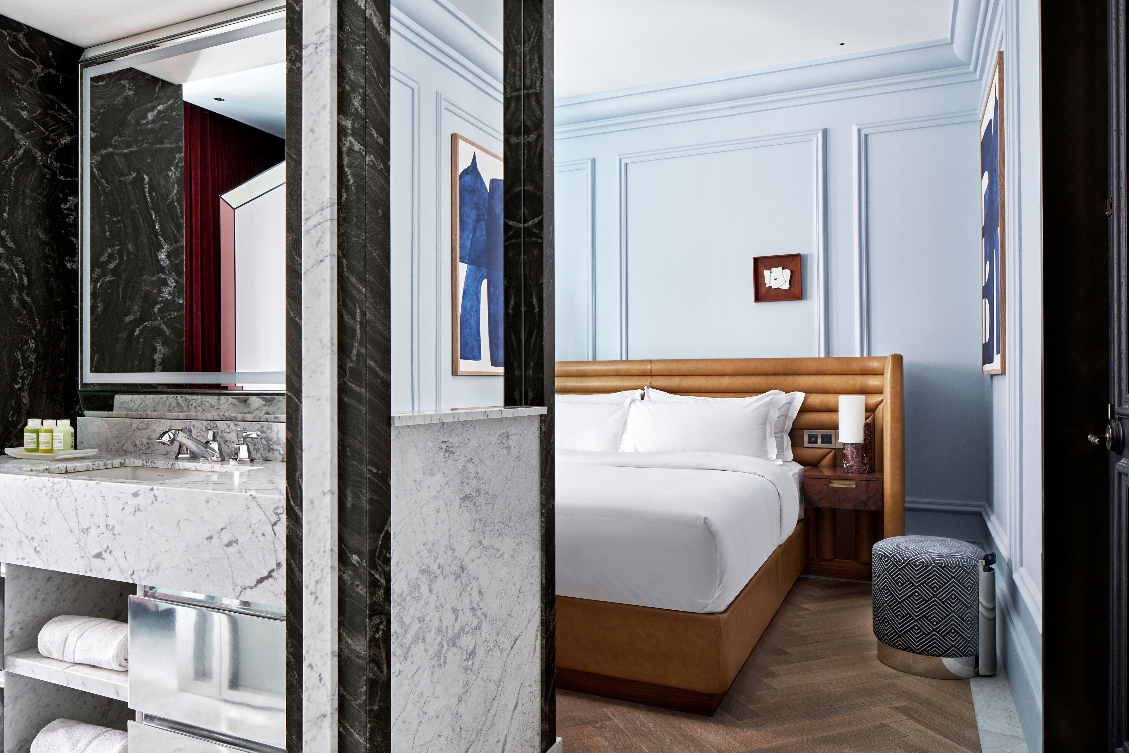 A hotel room with a marble bathroom, a wooden bed, and a nightstand with a lamp.