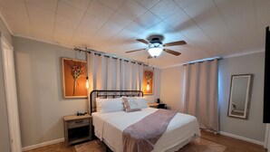 Quarto com cama, mesas de cabeceira, ventoinha no teto e espelho.