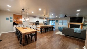Uma cozinha moderna com ilha central, área de refeições com cadeiras, um sofá e uma TV acima da lareira.