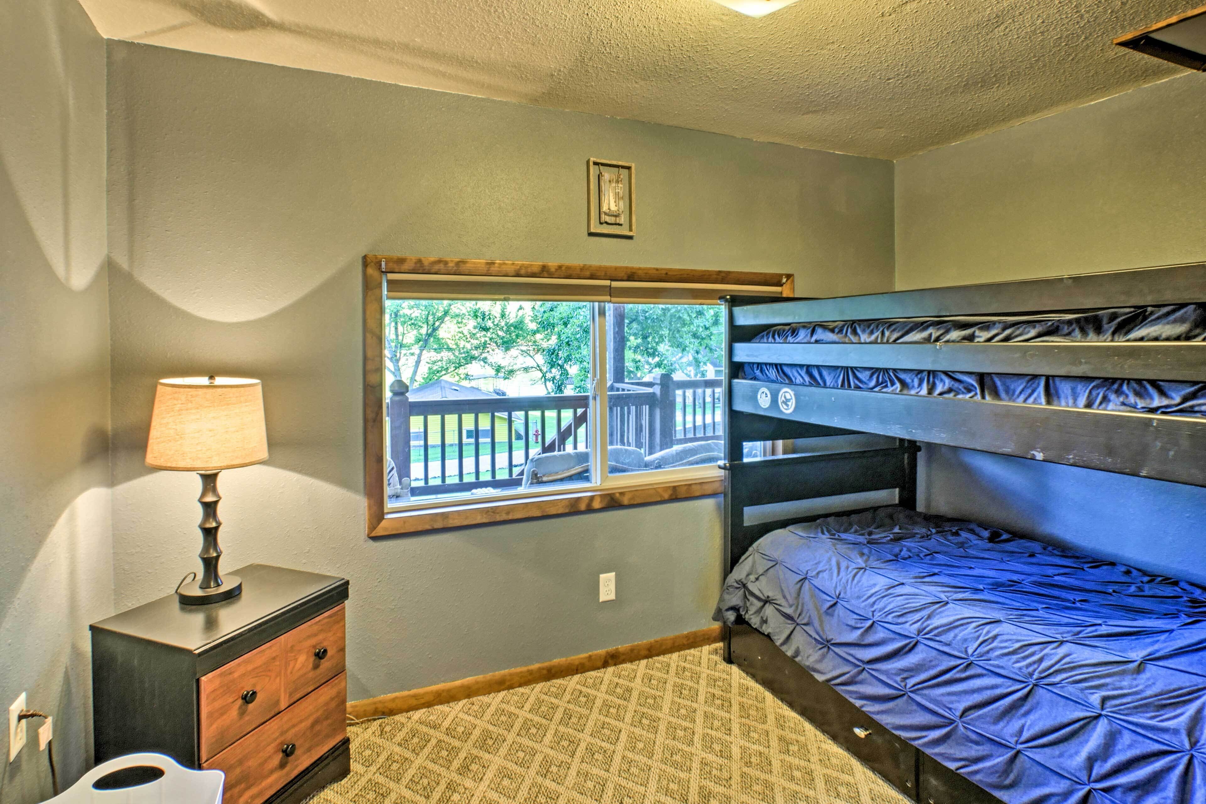 A bedroom with a bunk bed, a bedside table with a lamp, a window with a view of the outside, and a carpeted floor.