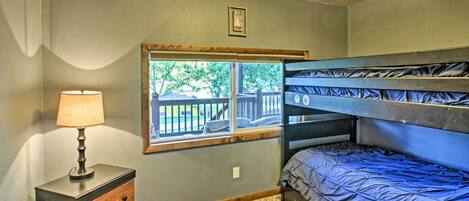 A bedroom with a bunk bed, a bedside table with a lamp, a window with a view of the outside, and a carpeted floor.