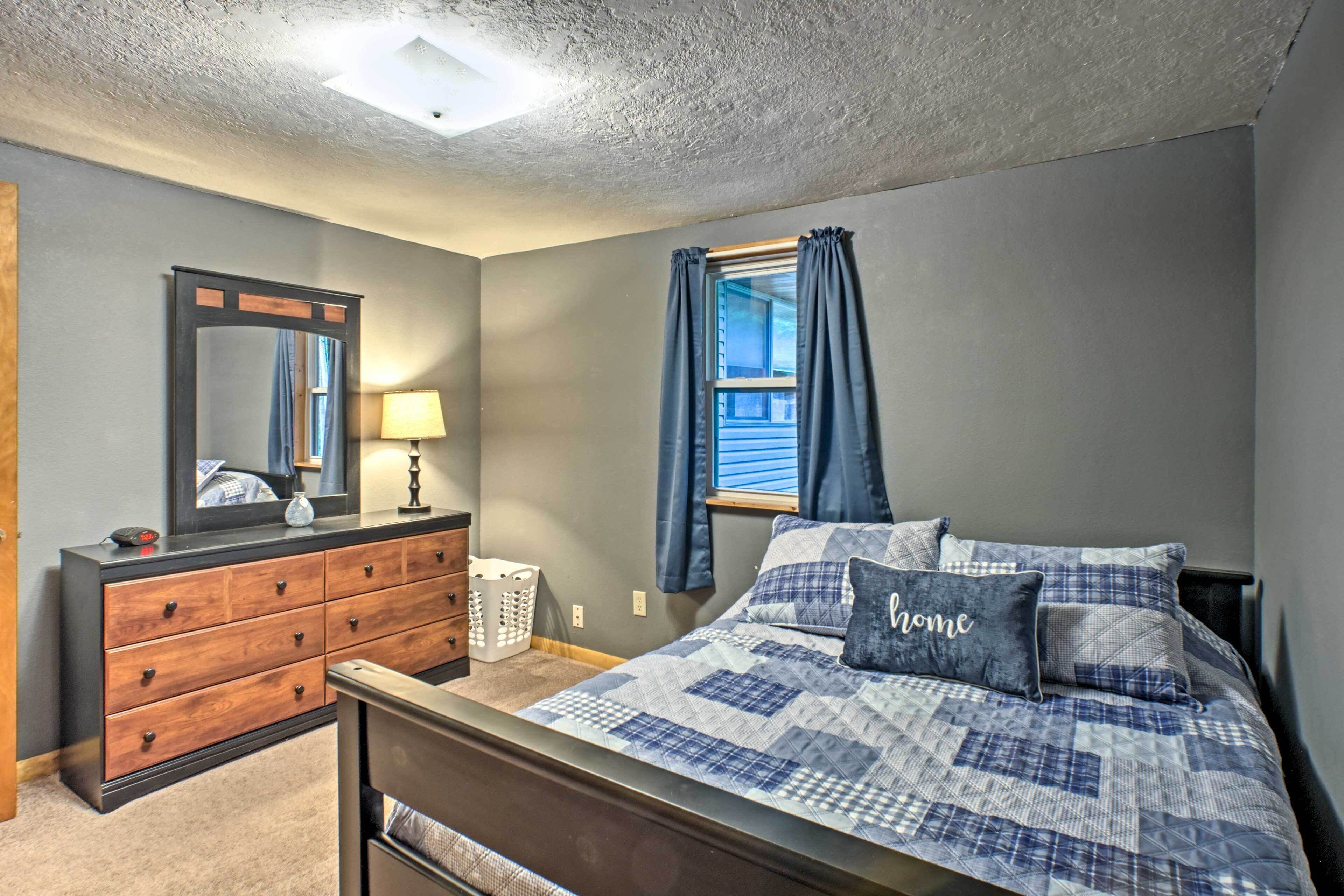 Een slaapkamer met een bed, een dressoir, een spiegel, een lamp en een raam met gordijnen.