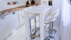 A modern kitchen with white cabinets, a stainless steel countertop, and a bar area with stools. - Luxury in downtown Debrecen (Debrecen)