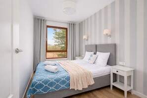 A bedroom with a bed, bedside tables, a window with curtains, and a view of trees.
