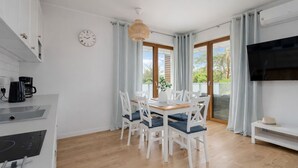 A modern kitchen with white cabinets, a coffee maker, and a dining area with a wooden table and white chairs. - HoliApart w Nautikka Park (Krynica Morska)