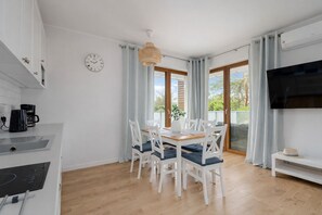 A modern kitchen with white cabinets, a coffee maker, and a dining area with a wooden table and white chairs.