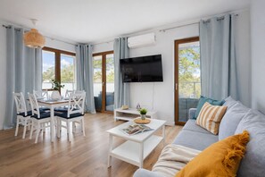 Una sala de estar moderna con comedor, televisión de pantalla plana y sofá con cojines.