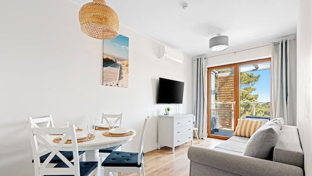 A modern living room with a dining area, a flat-screen TV, and a large window with a view. - HoliApart w Nautikka Park (Krynica Morska)