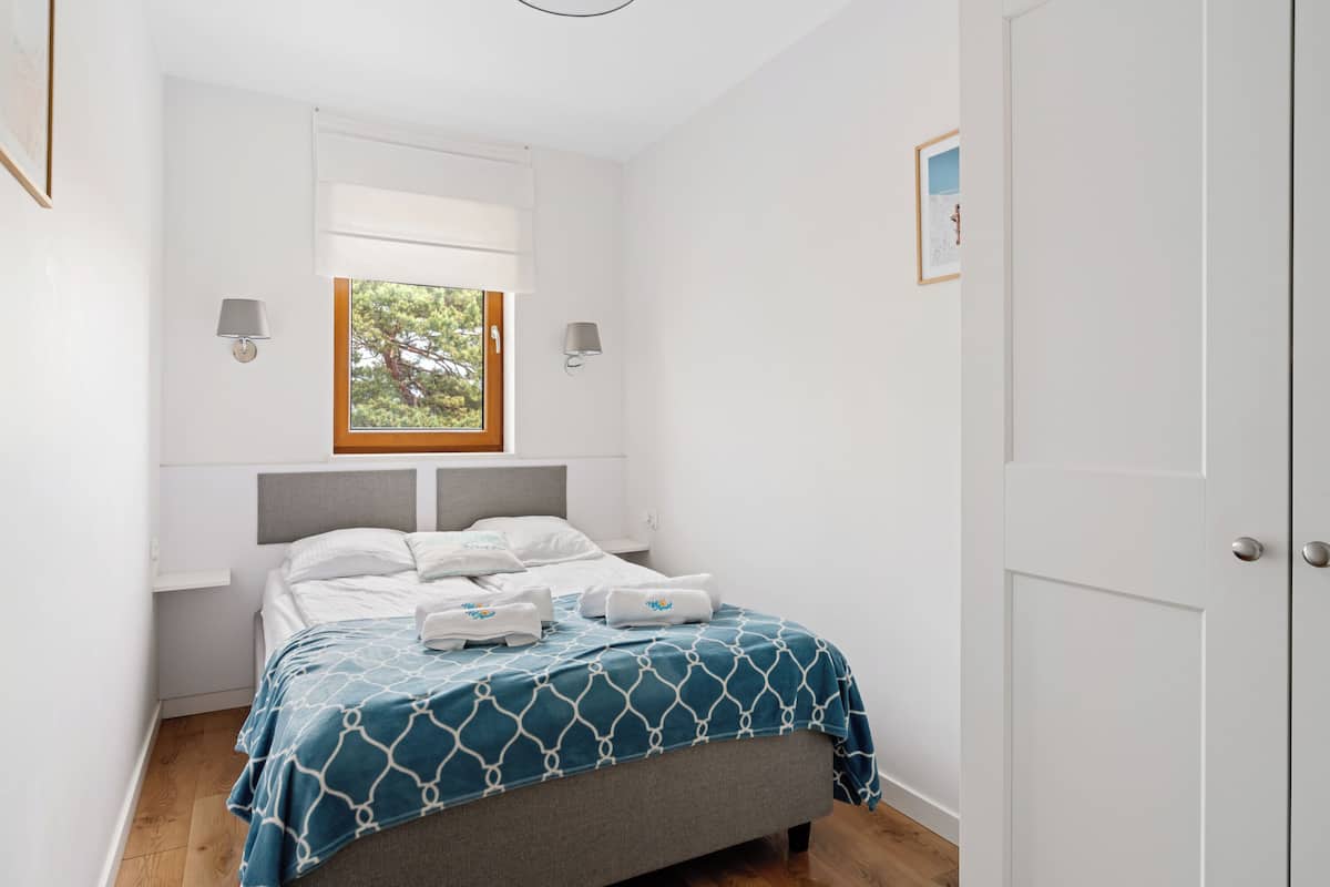 A bedroom with a bed, a window, two wall-mounted lamps, and a door.