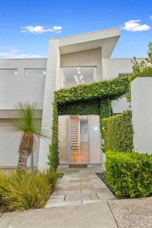 A modern building with a minimalist design, featuring a stone pathway leading to a glass door entrance.